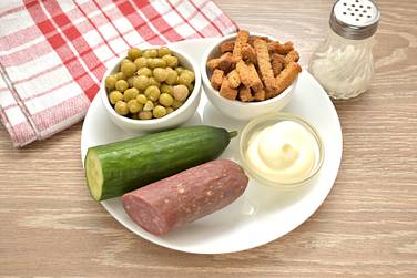 Чтобы приготовить салат с копчёной колбасой, горошком и сухариками, никаких ингредиентов отваривать заранее не нужно, поэтому сразу приступаем к измельчению продуктов