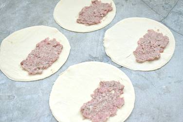 На одну сторону заготовки из теста помещаем столовую ложку мясной начинки и прижимаем её