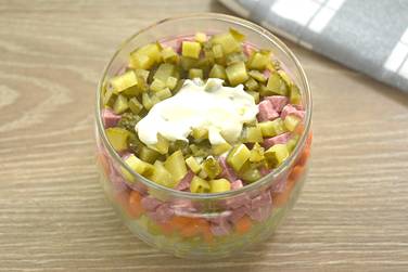 Маринованные огурчики шинкуем кубиками, укладываем на колбасу, закрываем майонезом